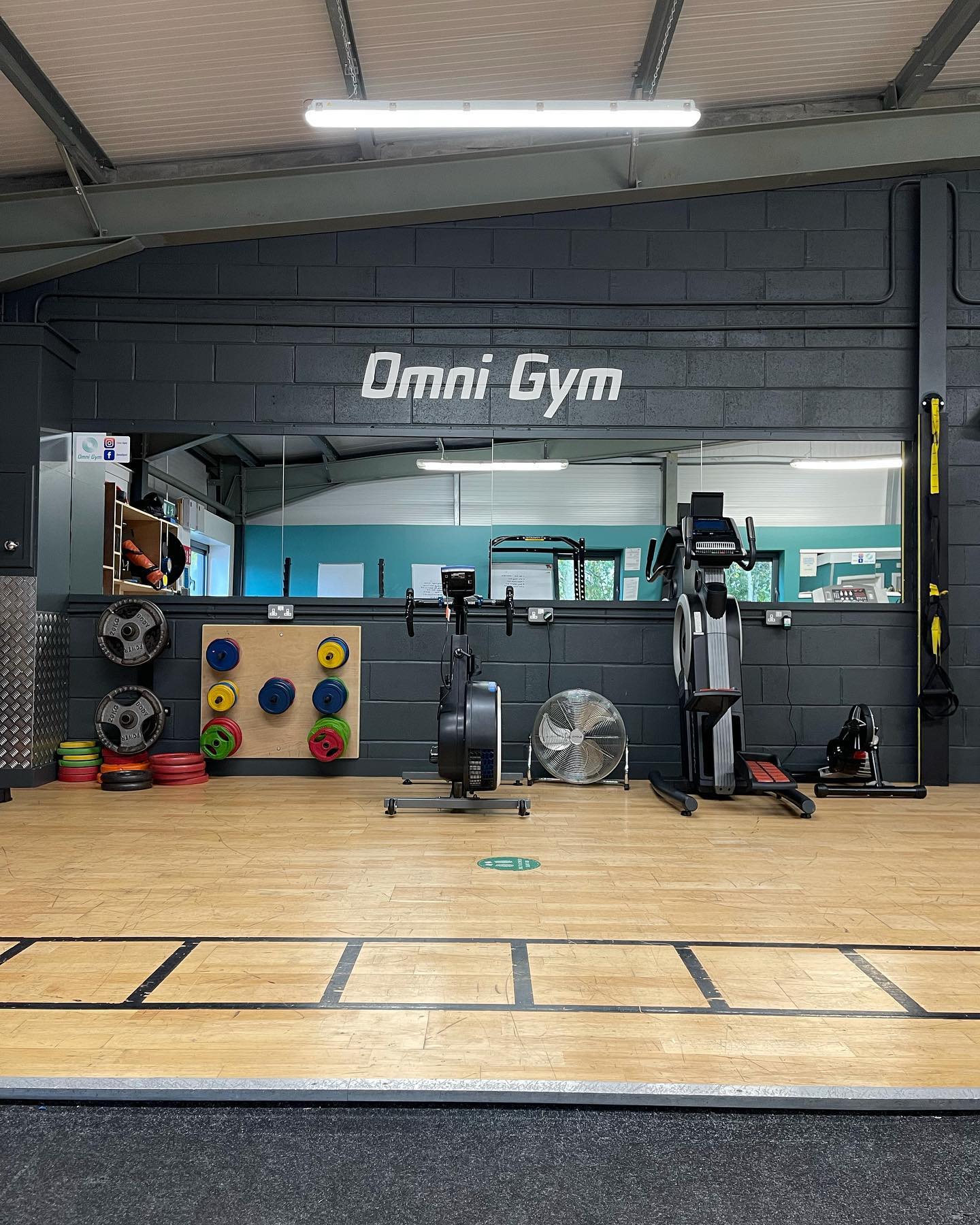 Gym floor with cardio equipment and white omni gym mural on wall